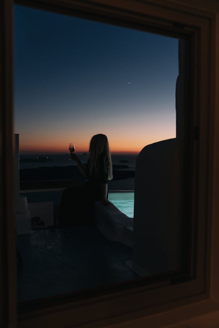 Woman on balcony with wine glass during sunset, offering a tranquil resort view.